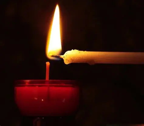 White candle lighting red glass candle in dark setting, close-up flame focus