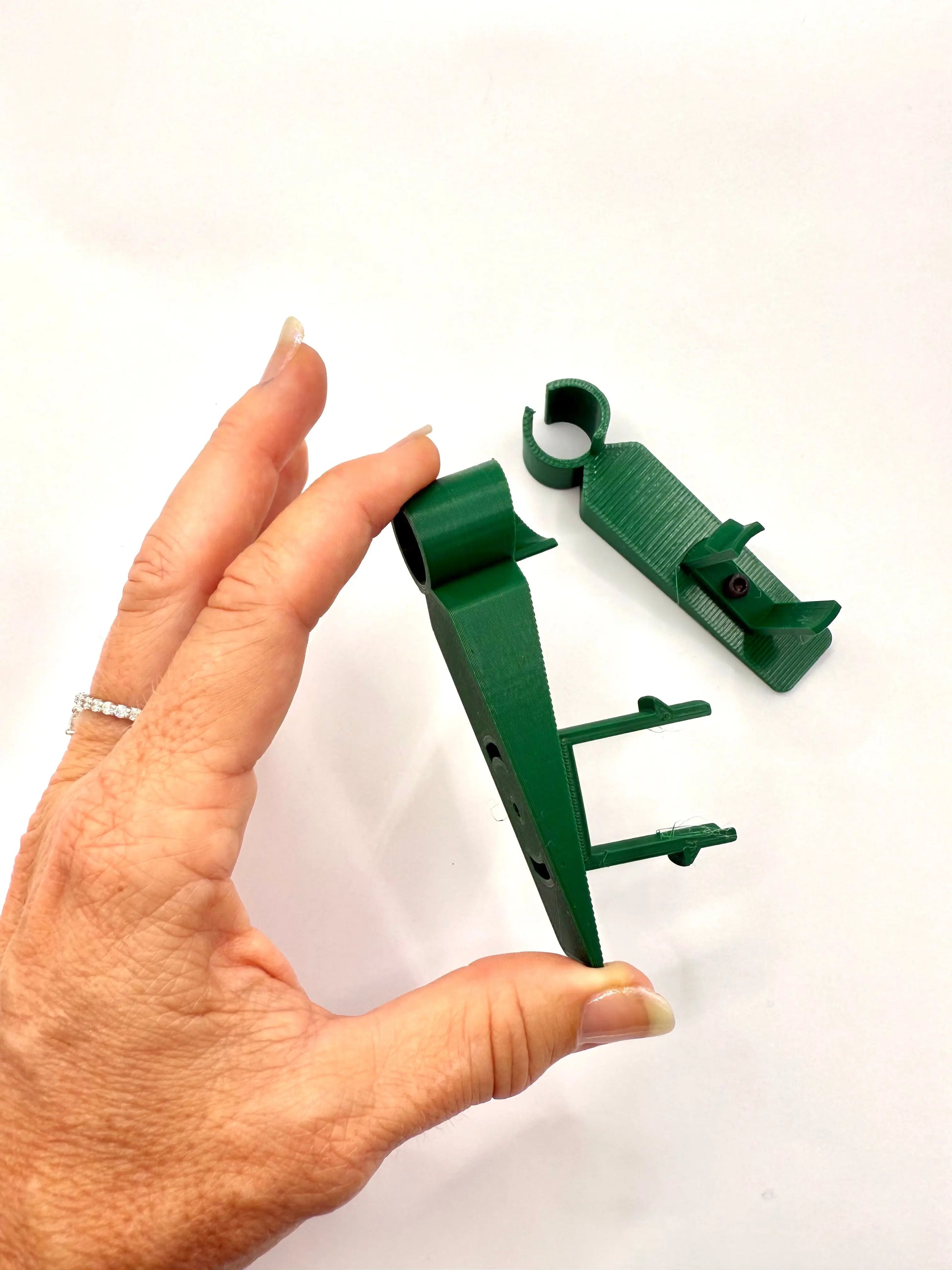 Hand holding green 3D printed plastic clip parts on white background